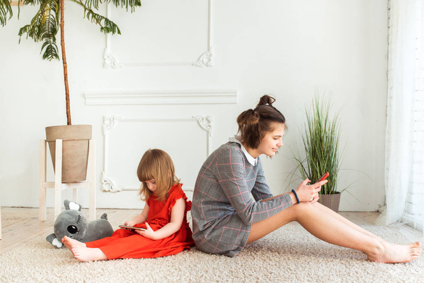 two sisters are sitting with their backs in a room on the floor of the house. They are looking at their telephone. communication and anti-communication of children. family values - Фото, изображение