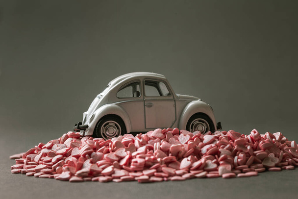 Retro speelgoed auto op de stapel van kleine roze hartvormige snoepjes op de grijze achtergrond. - Foto, afbeelding