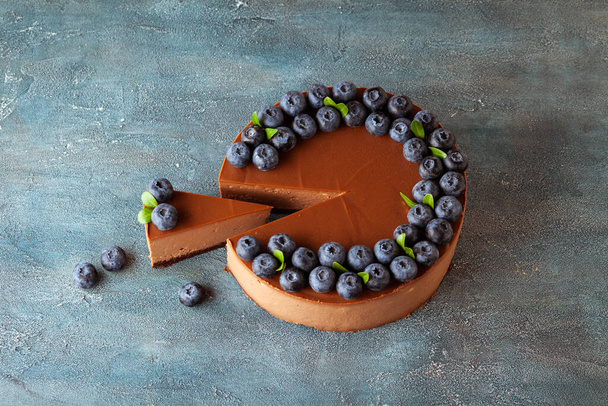 Chocolate brown cheesecake cut with fresh blueberries on vintage concrete background. - Foto, immagini