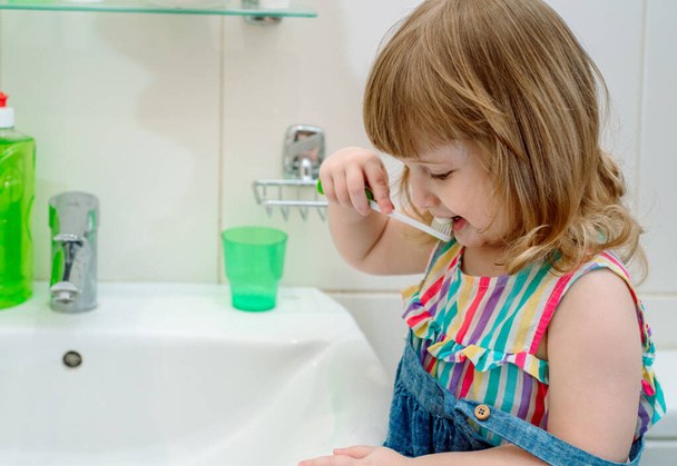 Little baby girl diligently brushing his teeth in the bathroom.Curly-haired girl laughs and shows clean teeth, child skin care - Foto, Imagen