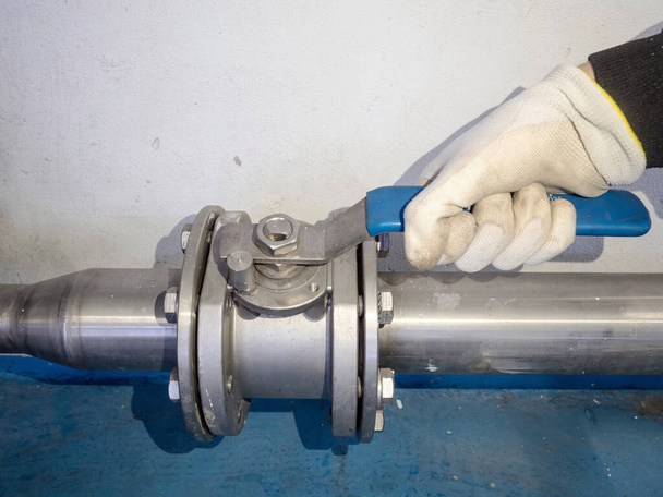 A mão do trabalhador com luva de segurança abriu válvula de esfera manual em tubo inoxidável de prata. pipeline industrial na fábrica.  - Foto, Imagem