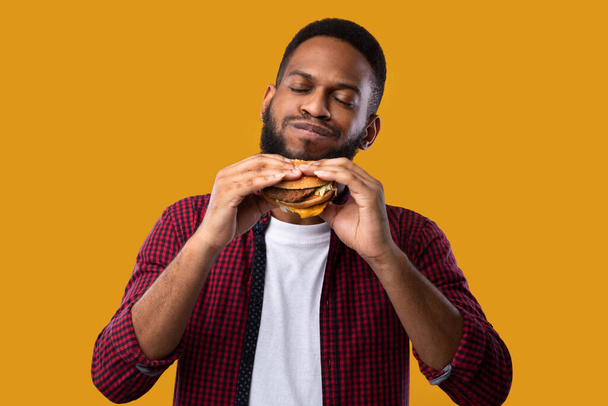Happy Afrikkalainen mies syö hampurilainen poseeraa yli keltainen studio tausta - Valokuva, kuva