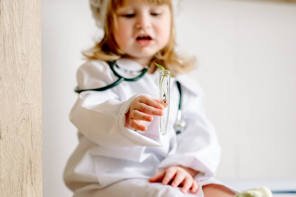Baby girl in the form of a doctor plays with a test tube. Research laboratory. Sprout in vitro. - Foto, Imagem