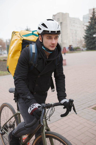 Vertical shot of a young delivery guy with thermo backpack riding bicycle - Φωτογραφία, εικόνα
