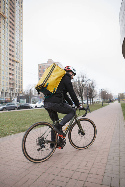 Vertical rear view shot of a deliveryman wearing helmet and thermo backpack, riding bicycle while working - Fotó, kép