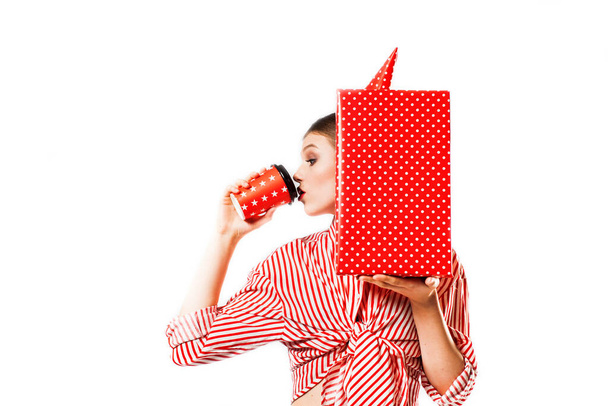 woman in a trendy striped red shirt with a lot of gift boxes.Surprised is drinking coffee. young lady holding white paper gift box with red ribbon.studio white. party, birthday or valentine day. - Valokuva, kuva