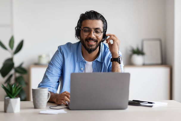 Enseñanza a distancia. Positivo joven árabe chico en auriculares viendo webinar en el ordenador portátil - Foto, Imagen