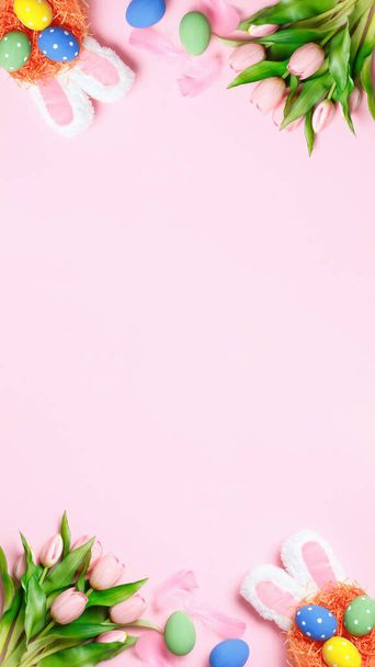 Easter eggs, tulips, bunny ears on a pink background. Greeting card with copy space flat lay. - Фото, изображение
