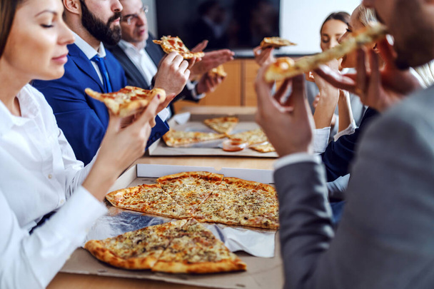 Skupina hladových obchodníků, kteří si dávají pizzu k obědu, zatímco sedí v zasedačce. - Fotografie, Obrázek