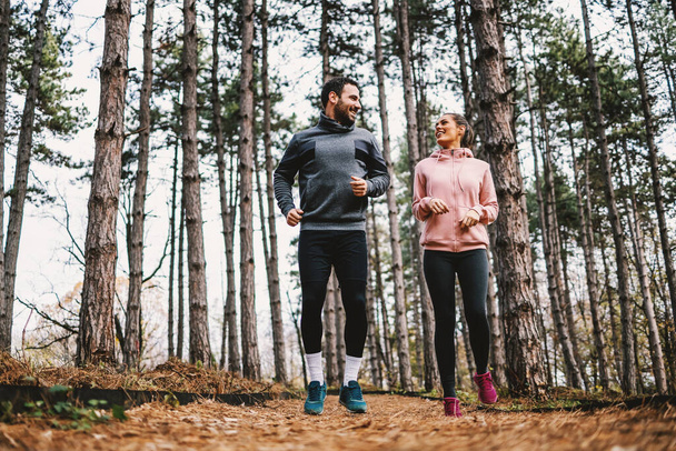 Pleine longueur du couple en forme courant à travers les bois à l'automne et se préparant pour le marathon. - Photo, image