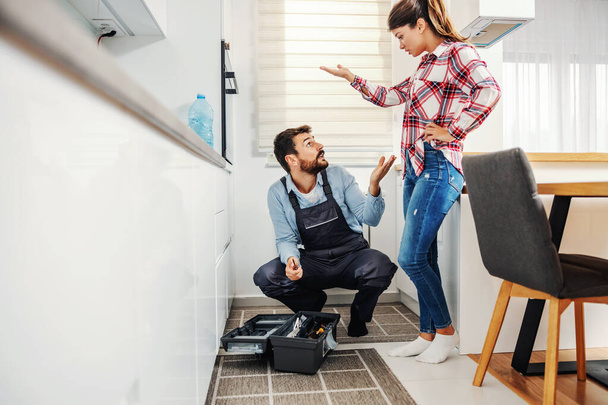 Woman standing in her kitchen with repairman and arguing with him. She is pointing at oven and asking him why is not repaired. - Foto, Imagen