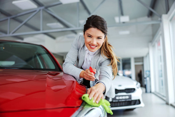 Lächelnde, aufgeräumte Autoverkäuferin reibt Auto mit Waschmittel und Tuch ein. Alles muss glänzend und sauber sein. - Foto, Bild