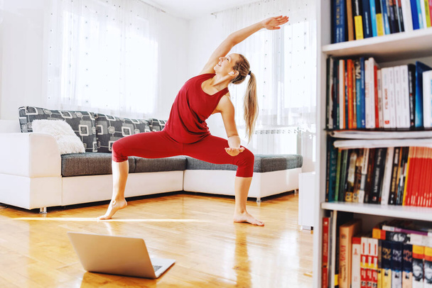 Усміхнений інструктор йоги стоїть в позі богині йоги і має онлайн-клас. Інтер'єр будинку
. - Фото, зображення