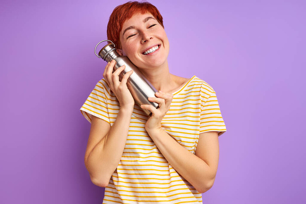 pleasant redhead woman with thermos isolated on purple background - Foto, immagini