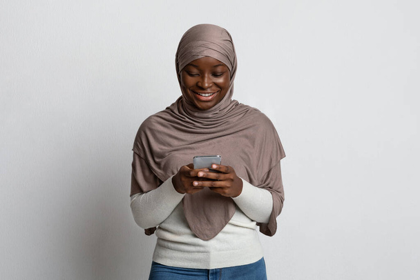 Мобільний зв'язок. Усміхнена чорна мусульманська леді в Headcarf Використовуючи смартфон
 - Фото, зображення