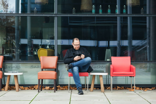 joven se sienta con un teléfono inteligente en un café al aire libre - Foto, Imagen