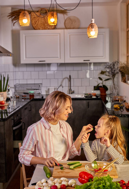 atractiva joven madre soltera haciendo una ensalada en la cocina con su hija - Foto, imagen