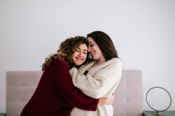 zwei weiße Mädchen mit braunen Haaren, die sich auf ihrem Bett umarmen. die Mädchen lächeln, als sie ihre Liebe zeigen - Foto, Bild
