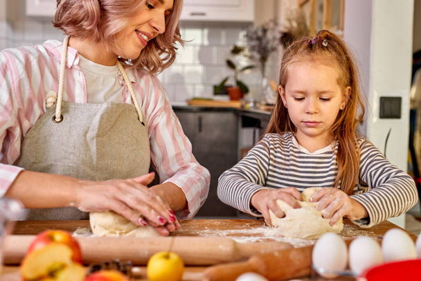 mom and daughter prepare flour baked goods on a table in the kitchen at home - Photo, image