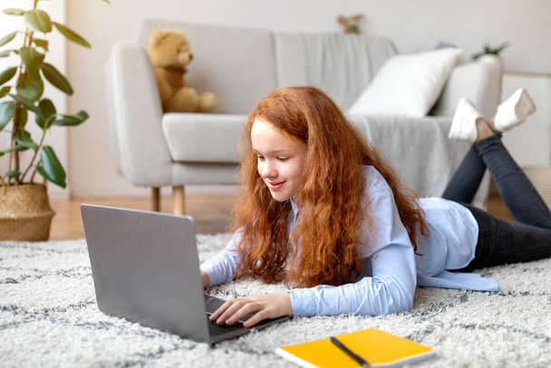 Mädchen liegt auf Teppich und benutzt ihren Laptop - Foto, Bild