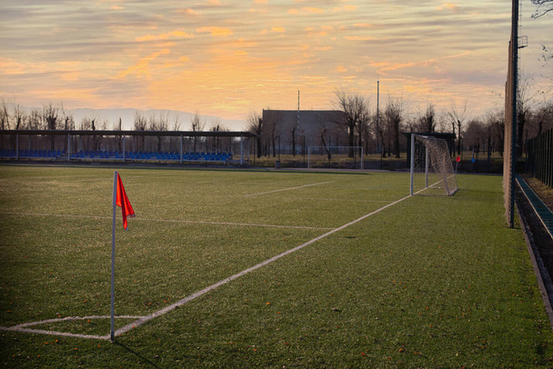 Rote Fahne auf dem Kunstrasen-Fußballplatz bei Sonnenuntergang - Foto, Bild
