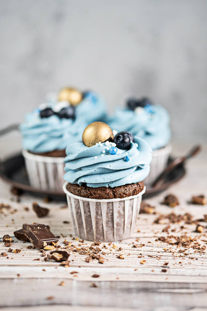 Several muffins or cupcakes with blue shaped cream and blueberrieson at white table. Rustic style copyspace. - Foto, afbeelding
