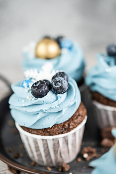 Several muffins or cupcakes with blue shaped cream and blueberrieson at white table. Rustic style copyspace. - Zdjęcie, obraz
