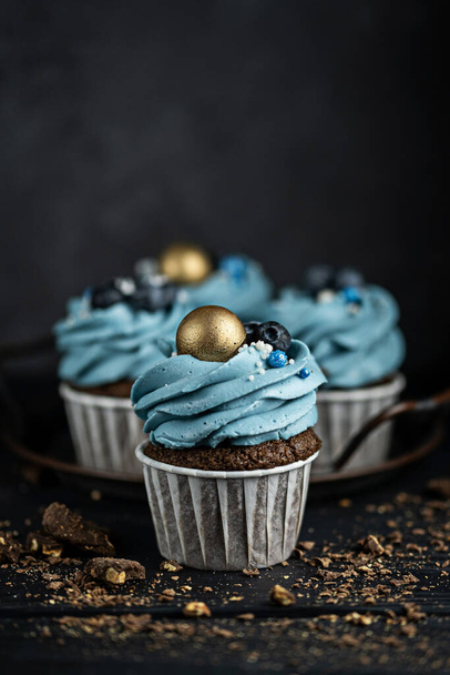 Several muffins or cupcakes with blue shaped cream and blueberrieson at black table. Rustic style copyspace. - Foto, afbeelding