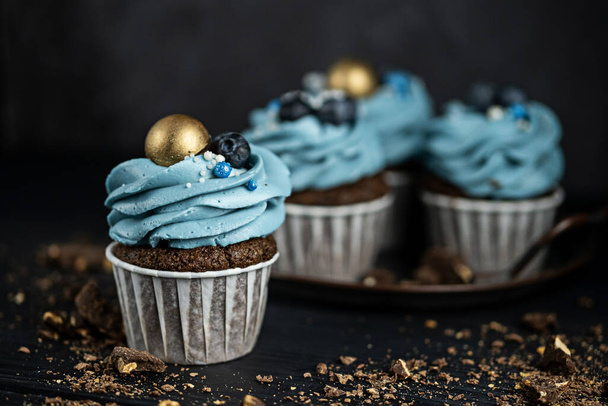Several muffins or cupcakes with blue shaped cream and blueberrieson at black table. Rustic style copyspace. - Valokuva, kuva