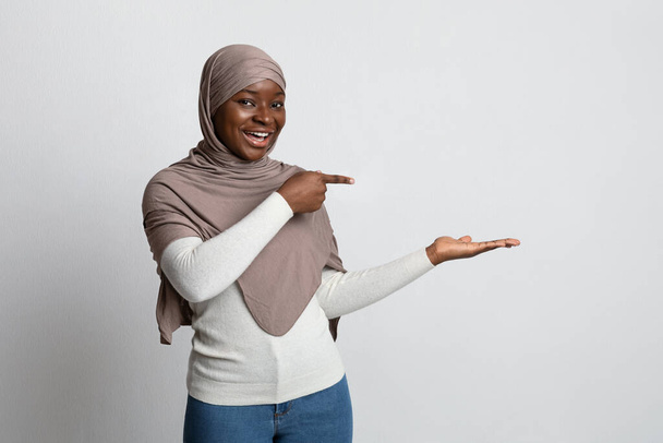 Check This. Excited Black Woman In Hijab Pointing At Her Empty Palm - Fotó, kép