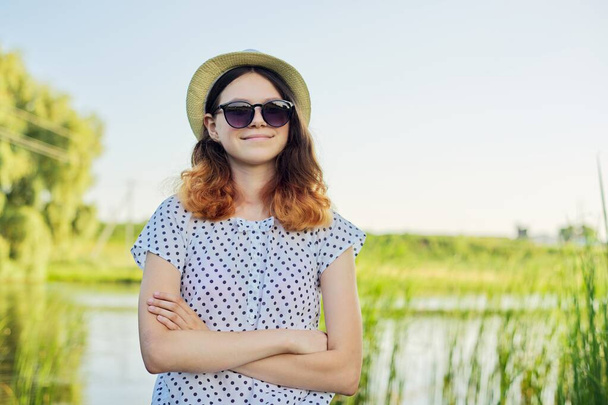 Outdoor country portrait of teenage girl in hat sunglasses near pond in the reeds - Fotó, kép