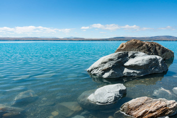 Nagy sziklák a szürke köves tó szélén és türkiz kék víz hó takarmány festői tó Pukaiki Dél-szigeteken Új-Zéland. - Fotó, kép