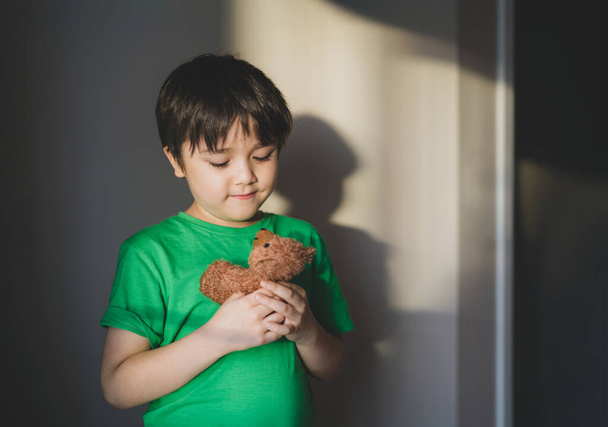 Kid playing teddy bear hiding in the shade of the wall in vintage tone,Yong boy playing with toy alone, Child having fun and relaxing at home on weekend,New normal lifestyle, Positive children concept - Photo, Image
