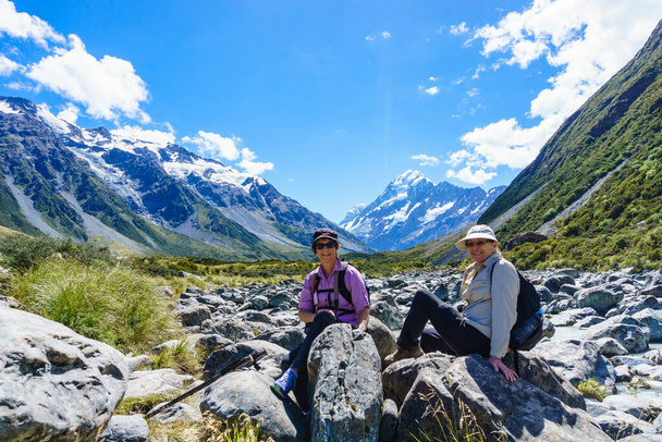Mount Cook Új-Zéland - Február 16 2015; Hooker Valley pálya a turisták, hogy egy kis szünetet ül a sziklákon egy nagy séta között hegyi lejtők. - Fotó, kép