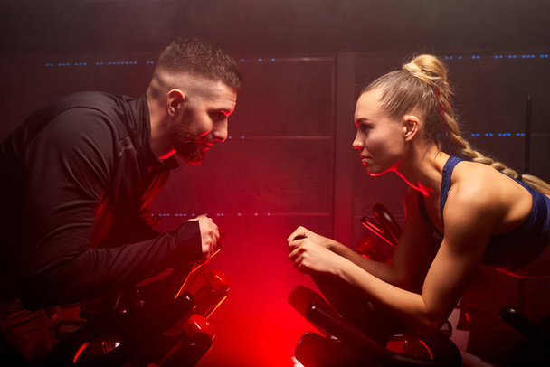 fitness workout woman and man training on smart stationary bike indoors, sport competition - Foto, afbeelding