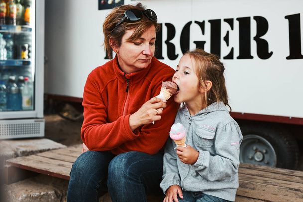Anne ve kızı dondurma yiyorlar yaz tatillerinde yemek kamyonunun önünde oturuyorlar. - Fotoğraf, Görsel