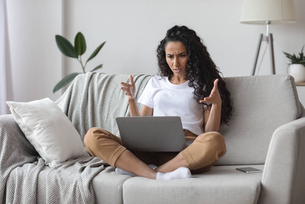 Öfkeli kadın dizüstü bilgisayara bakıp el kol hareketi yapıyor. - Fotoğraf, Görsel