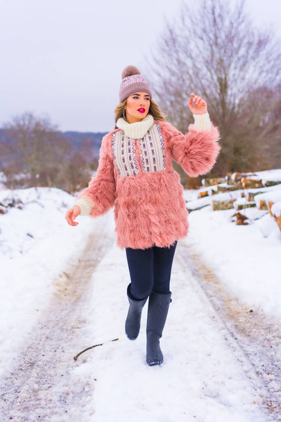 Young blonde girl in pink fur jacket, winter boots and a purple hat in the snow. Walking on a snow-filled path, lifestyle - Foto, immagini