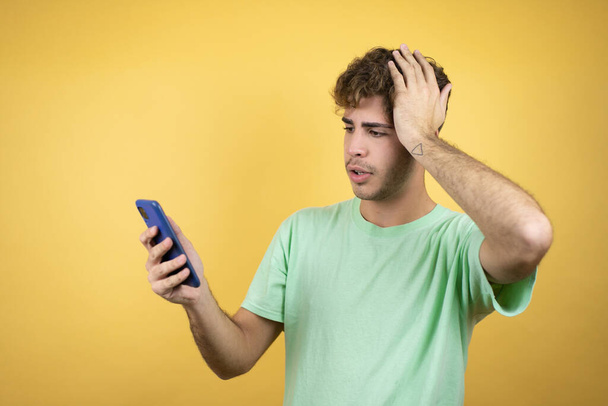 Jóképű férfi zöld alkalmi pólót visel sárga háttér felett csevegés telefonon egy aggódó kifejezés - Fotó, kép