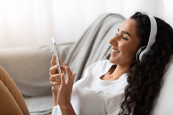 Boldog fiatal nő fülhallgatóban filmet néz telefonon - Fotó, kép