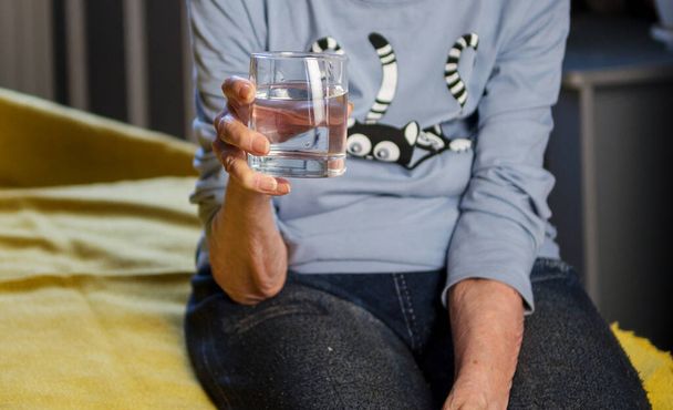 Yaşlı bir kadın ilaç içmek için elinde su tutuyor.. - Fotoğraf, Görsel
