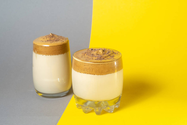 Due bicchieri di caffè dalgon con schiuma lussureggiante su uno sfondo grigio-giallo, Trendy bevanda coreana. - Foto, immagini
