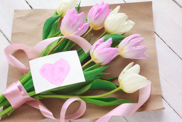Dámský den. kytice tulipánů na bílém dřevěném pozadí s kartou se srdcem. selektivní zaměření. - Fotografie, Obrázek
