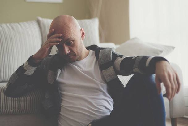 Un homme déprimé est assis sur le sol du salon, couvrant son visage de sa main.. - Photo, image