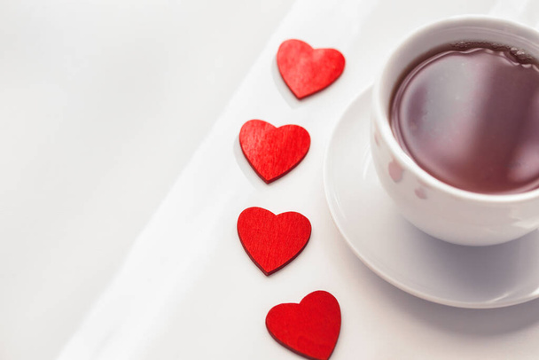 Top vista figurinos em forma de coração vermelho com xícara branca de chá no fundo claro. Bom dia com conceito de bebida quente. Espaço para SMS. Toneladas - Foto, Imagem