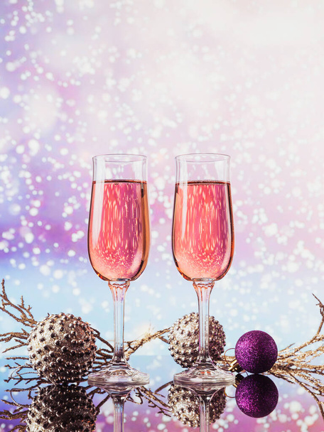 Two glasses of rose champagne and Christmas or New Year decoration with light snow bokeh on background. Romantic dinner. Winter holiday concept. - Foto, imagen