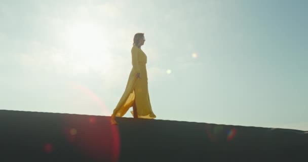 黄色のドレスでスタイリッシュな女性歩く上の砂の砂丘でスローモーション - 映像、動画