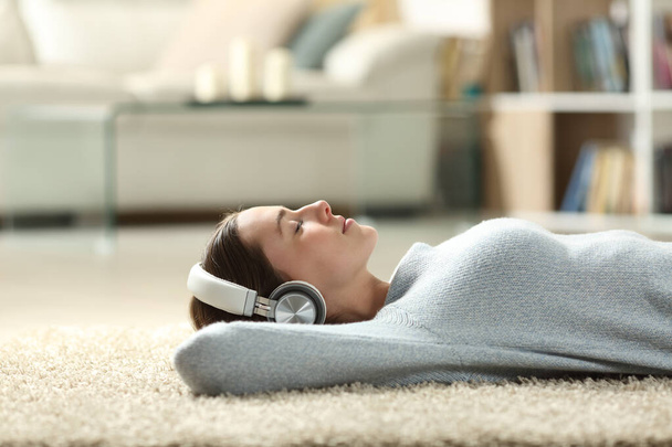 Retrato de una mujer relajada escuchando música con auriculares acostados en una alfombra en casa - Foto, imagen