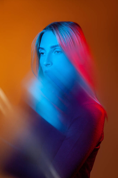 Jeune femme réfléchie avec lumière bleue sur le visage dans un studio orange - Photo, image