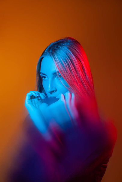 Thoughtful young lady with blue light on face in orange studio - Photo, image